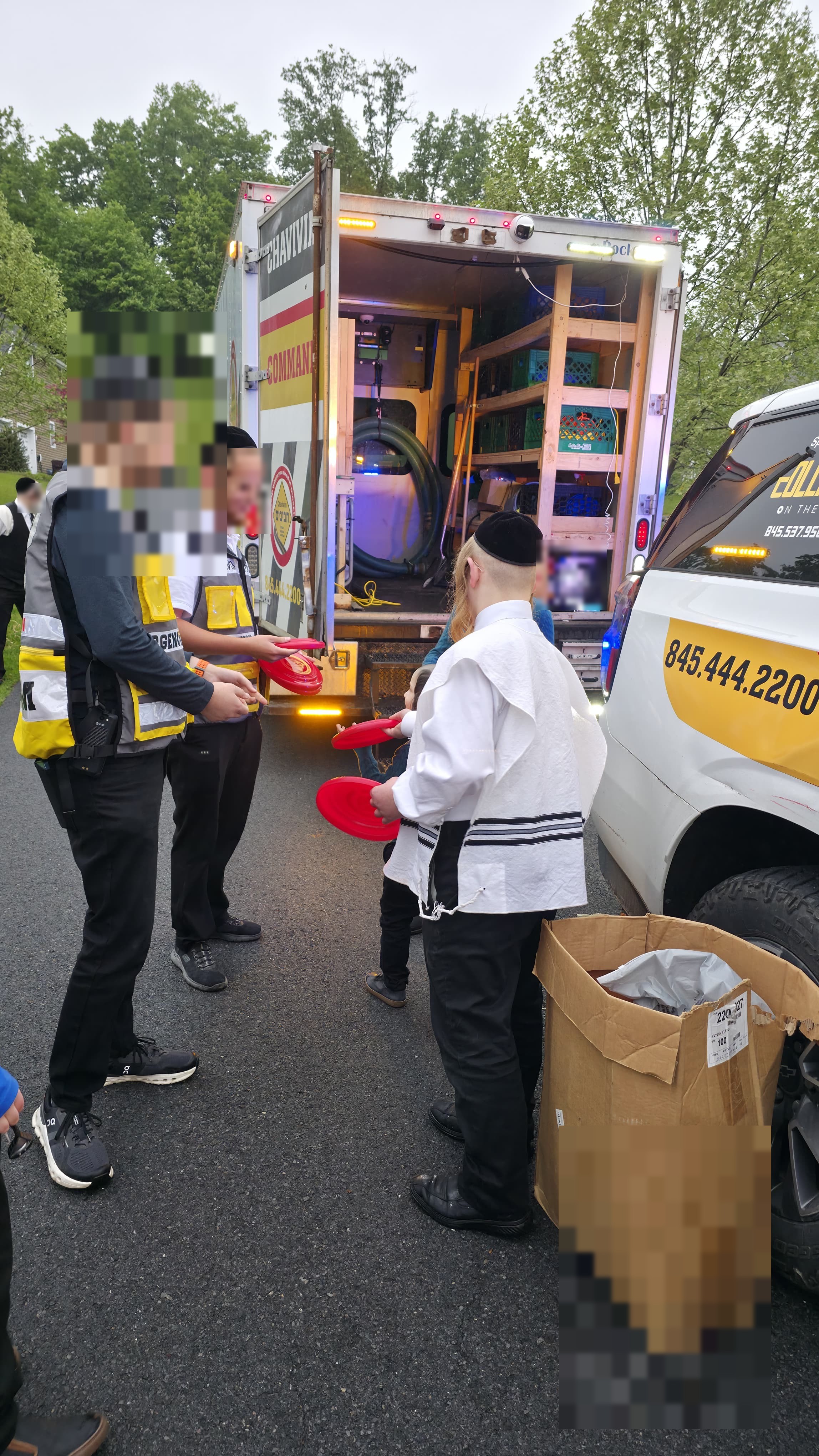Chavivim members handing red frisbees to children at the open rear of the KJ-500 Command Center truck