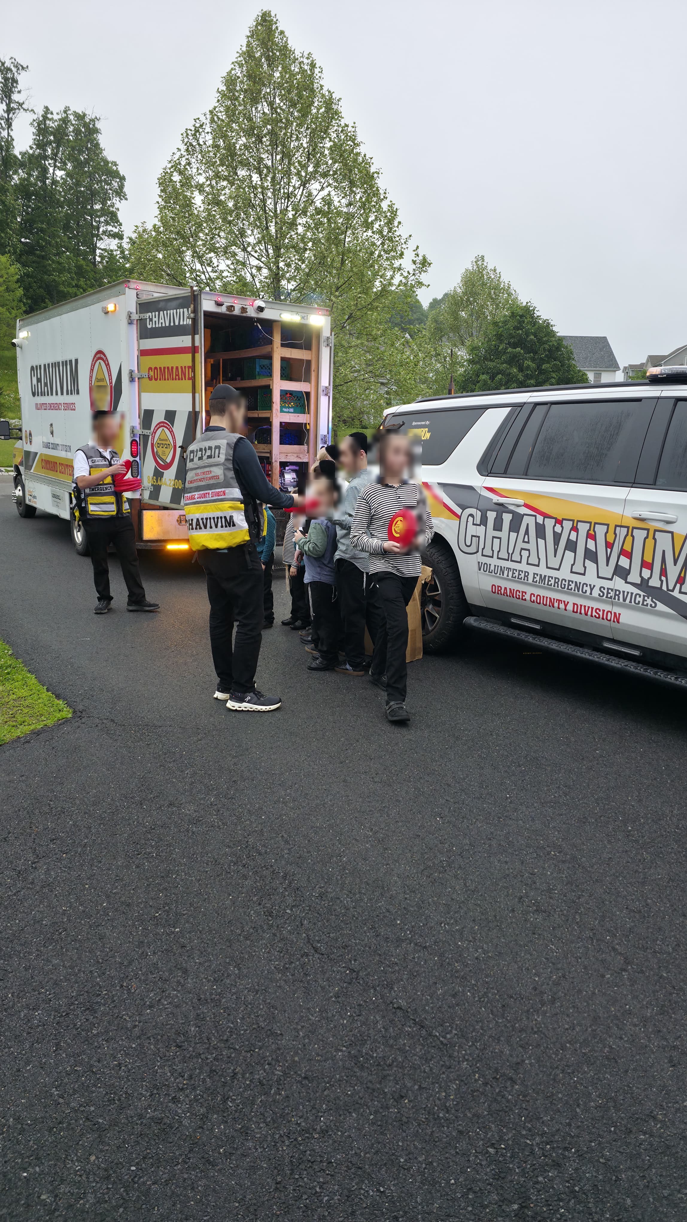 Orange County Chavivim members handing out frisbees to children beside the KJ-500 Command Center truck and KJ-501 fly car