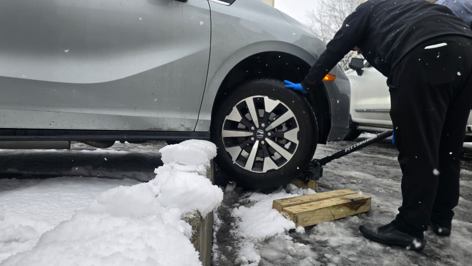 Chavivim member using a floor jack and wooden blocks to lift the wheel off the curb