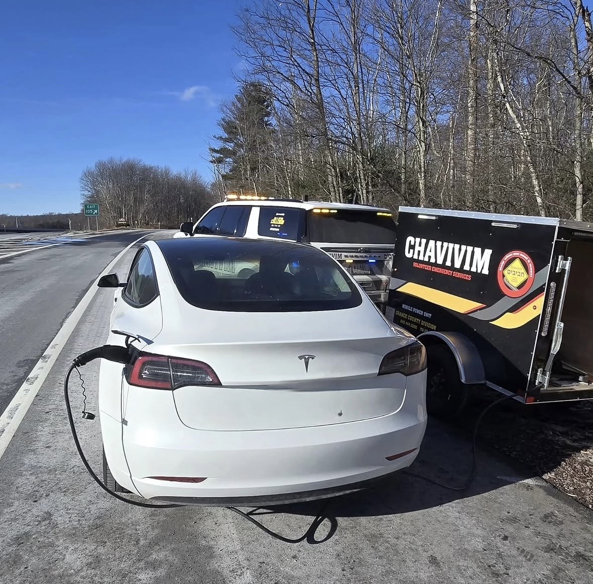 White Tesla Model 3 plugged into the Chavivim EV1 mobile charging trailer on the shoulder of Route 17 at Exit 105