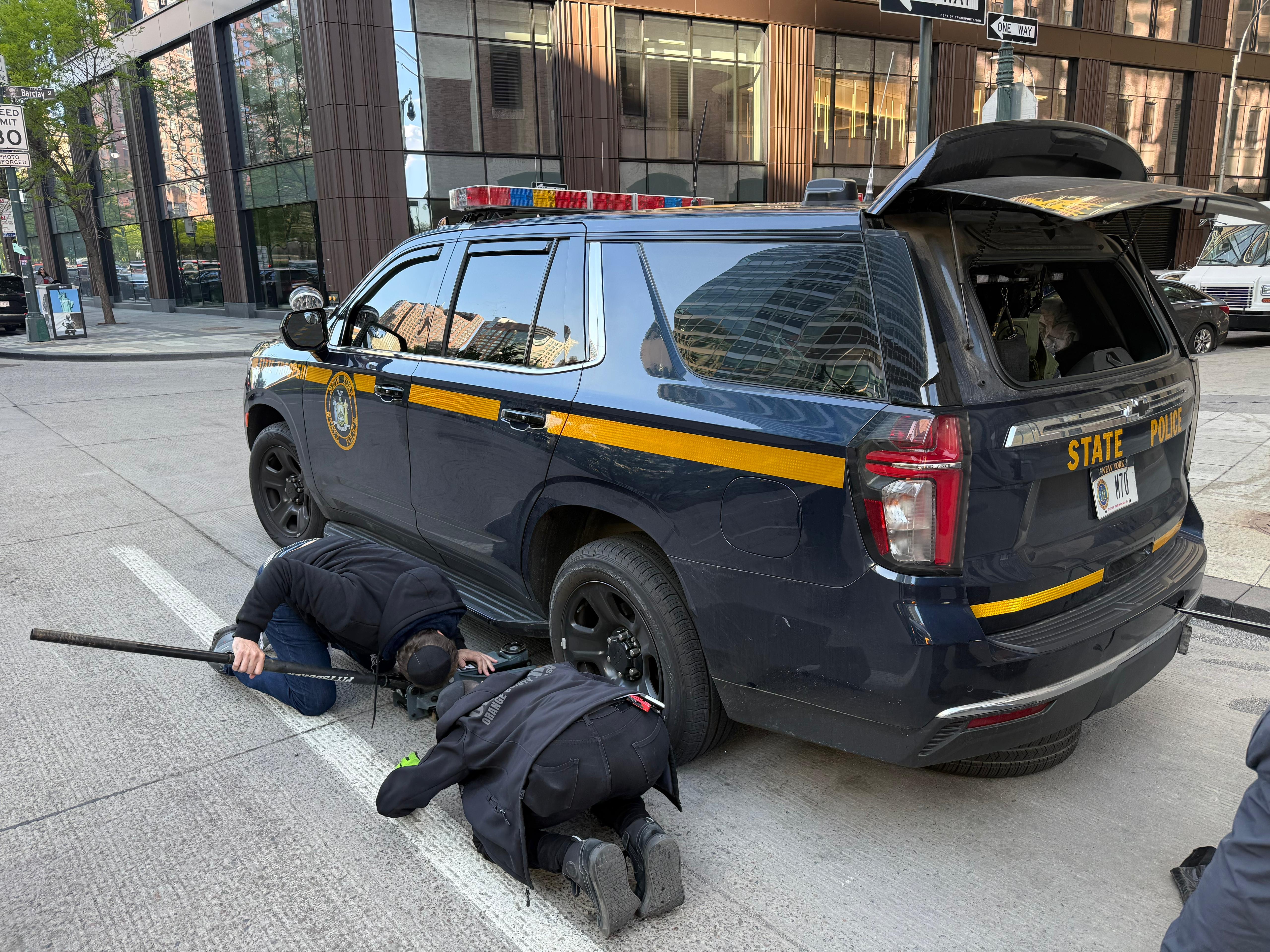 Two Chavivim members flat on the ground under the rear of the NYSP SUV working the tire change