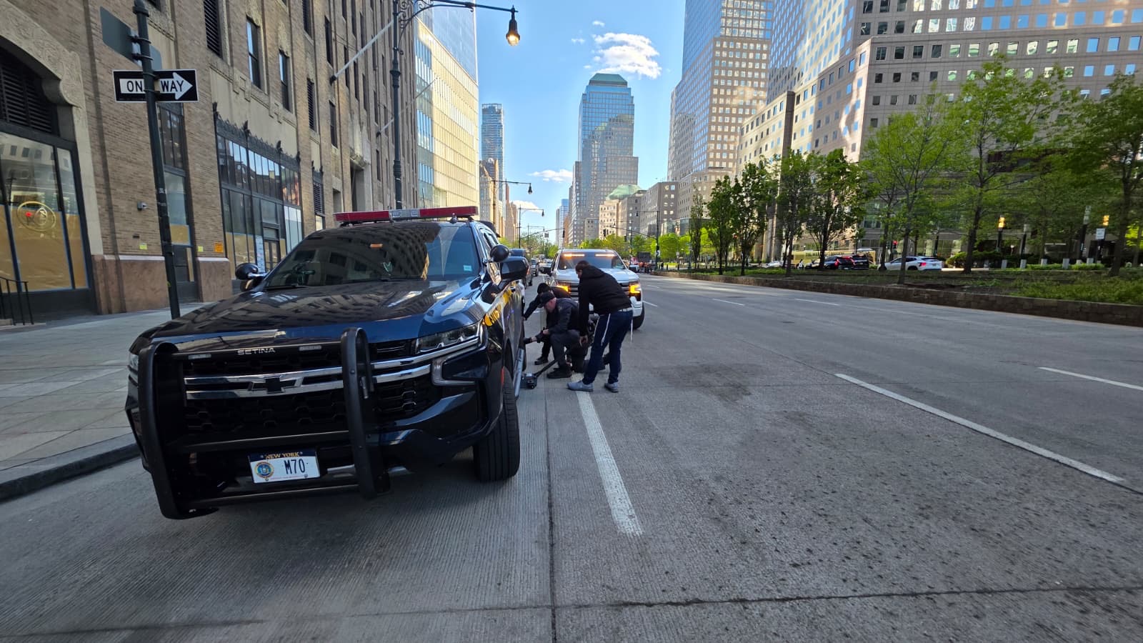 NY State Police SUV with plate M70 stopped on a Lower Manhattan street with the Financial District skyline in the background