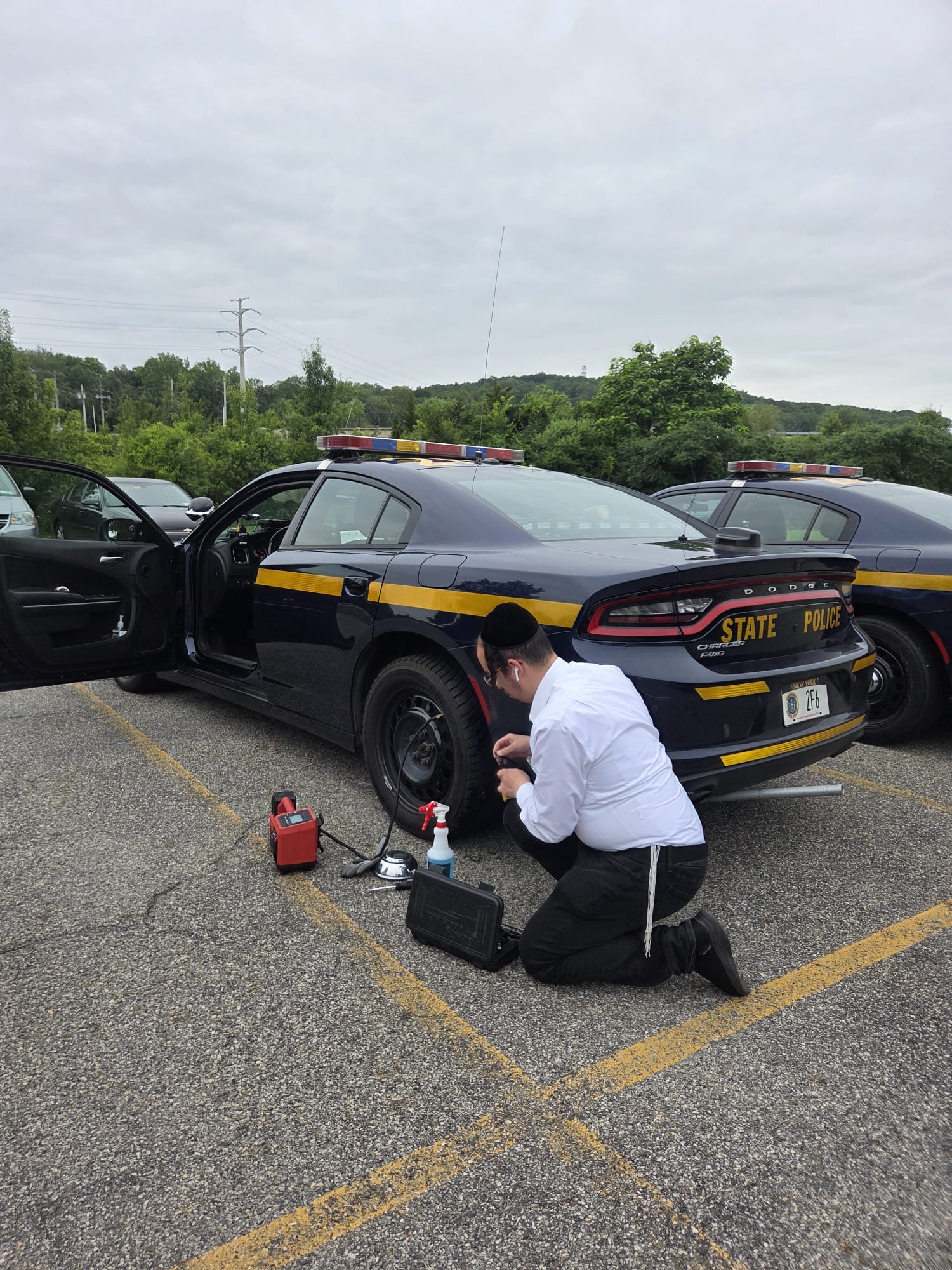 Chavivim member kneeling beside a NY State Police patrol car working on the flat tire