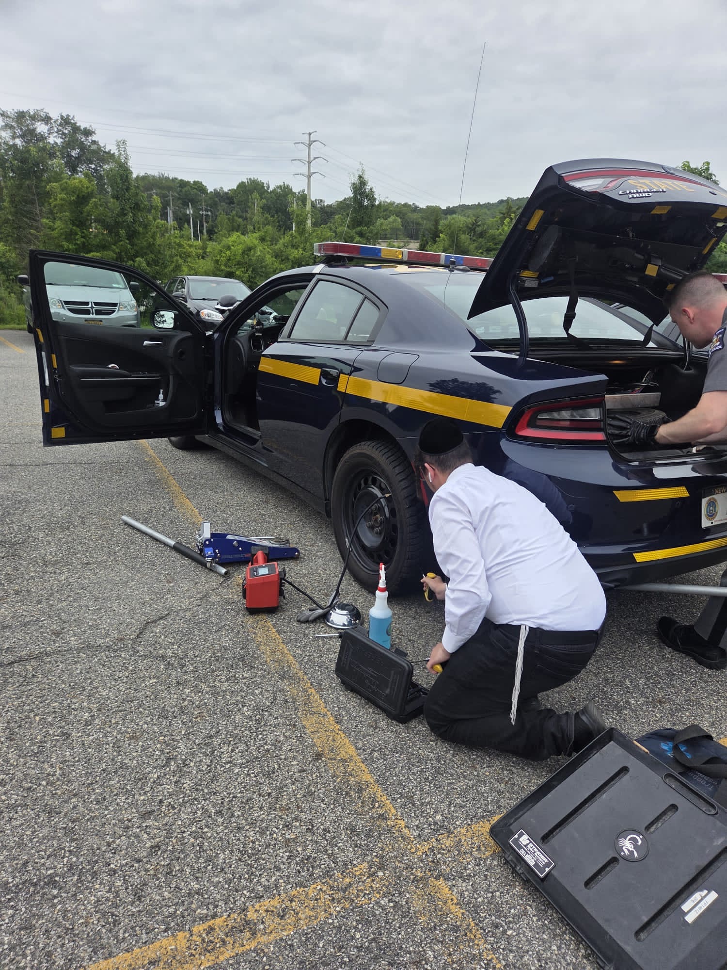 Chavivim member changing a flat tire on a NY State Police patrol car in Monroe with a trooper at the trunk