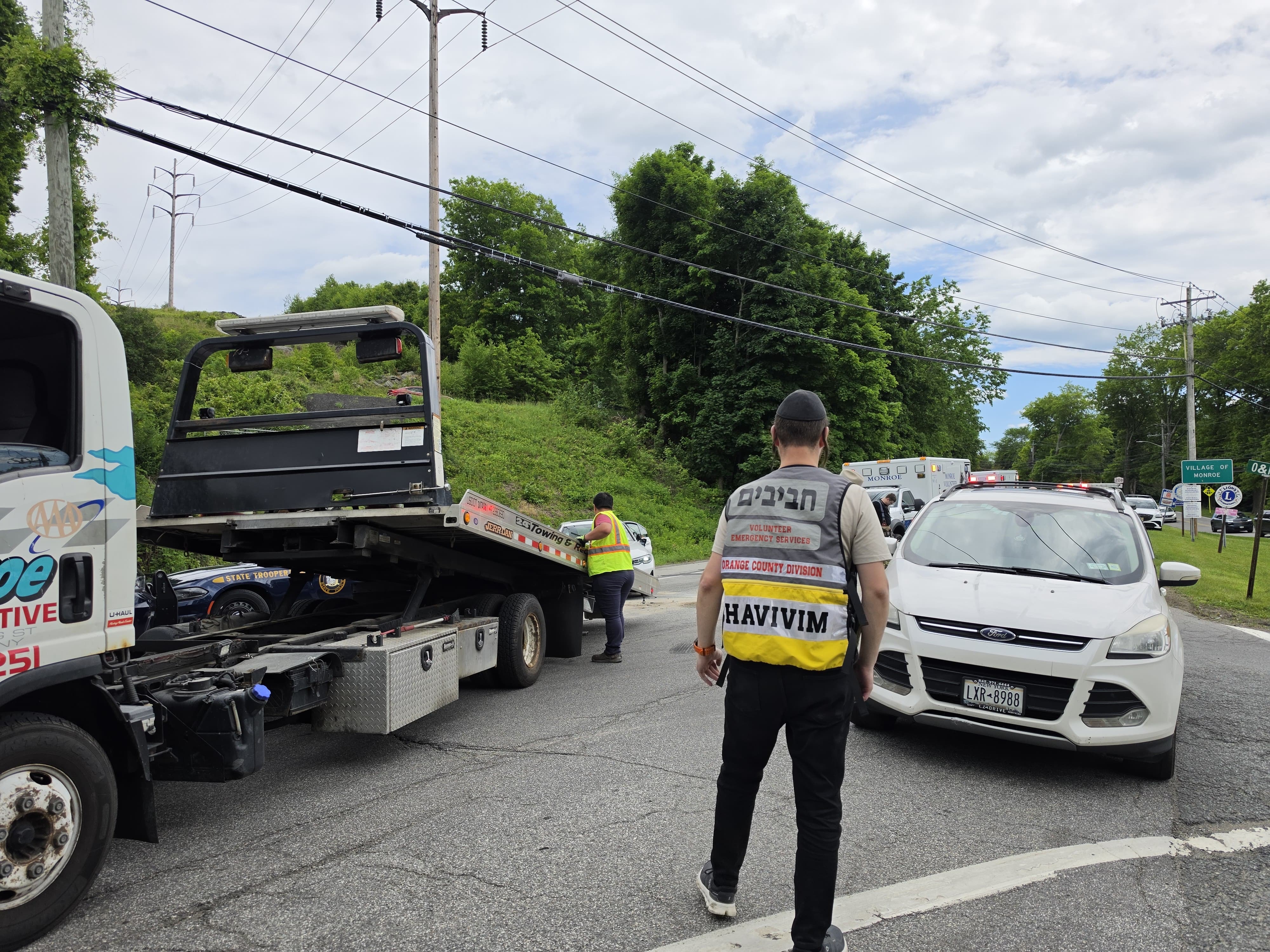 A Chavivim member directing traffic in the road as the Monroe Automotive flatbed loads a vehicle near a white SUV