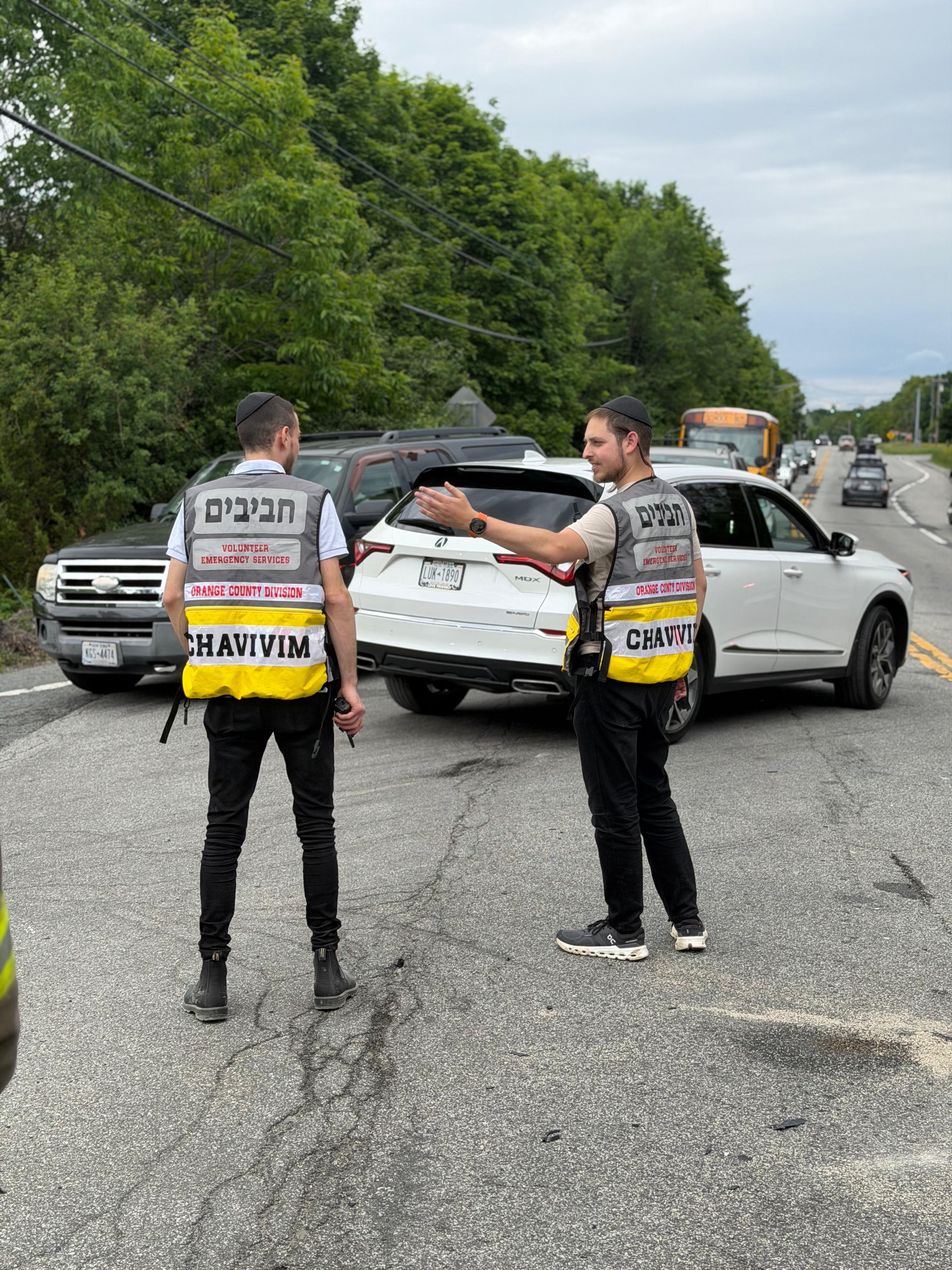 A Chavivim member in a hi-vis vest and a New York State Trooper in the road beside a Chavivim vehicle at the second scene