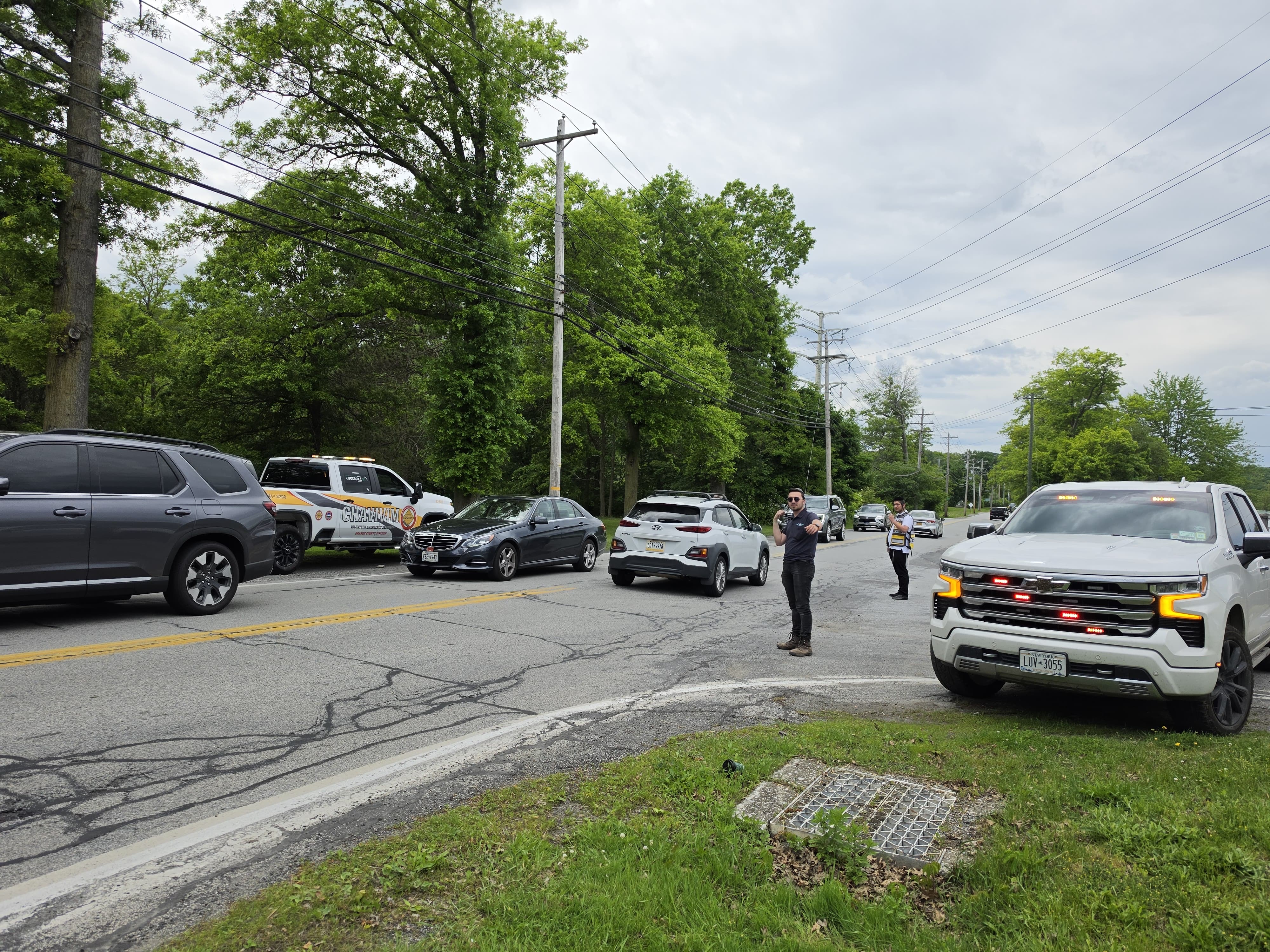 Wide view of the intersection with vehicles lined up and the KJ-503 pickup staged as members direct traffic